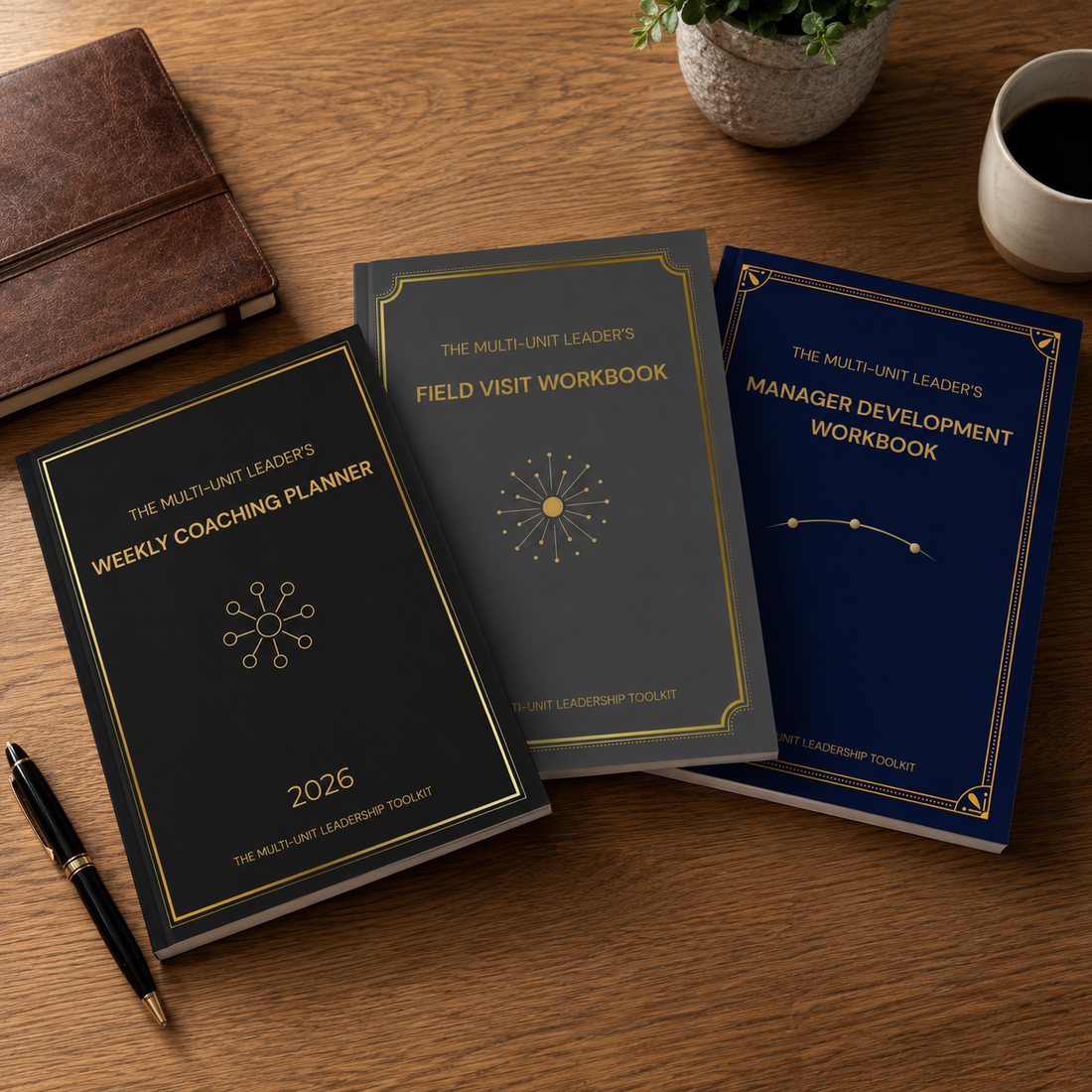 Three field-coaching workbooks on a wooden desk: the Weekly Coaching Planner, Field Visit Workbook, and Manager Development Workbook, in black, grey, and navy with gold detailing.